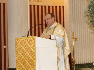 D. Alfonso, párroco, con casulla blanca y dorada leyendo en el ambón durante la celebración de una misa.